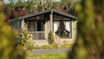 Une cabane dotée d’une terrasse en bois, de grandes fenêtres et d’un petit porche.