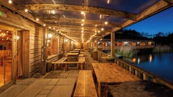 An outdoor wooden deck with tables and benches, overlooking a body of water.