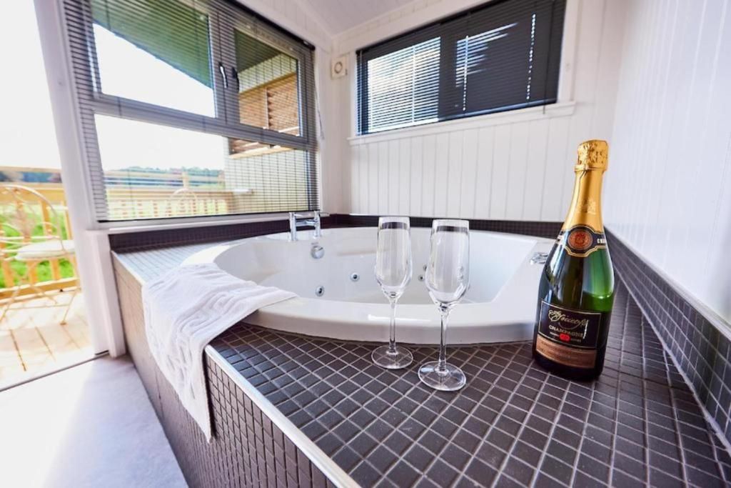 Un bain à remous avec deux verres et une bouteille de champagne posés sur une surface carrelée.