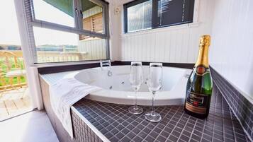 Un bain à remous avec deux verres et une bouteille de champagne posés sur une surface carrelée.