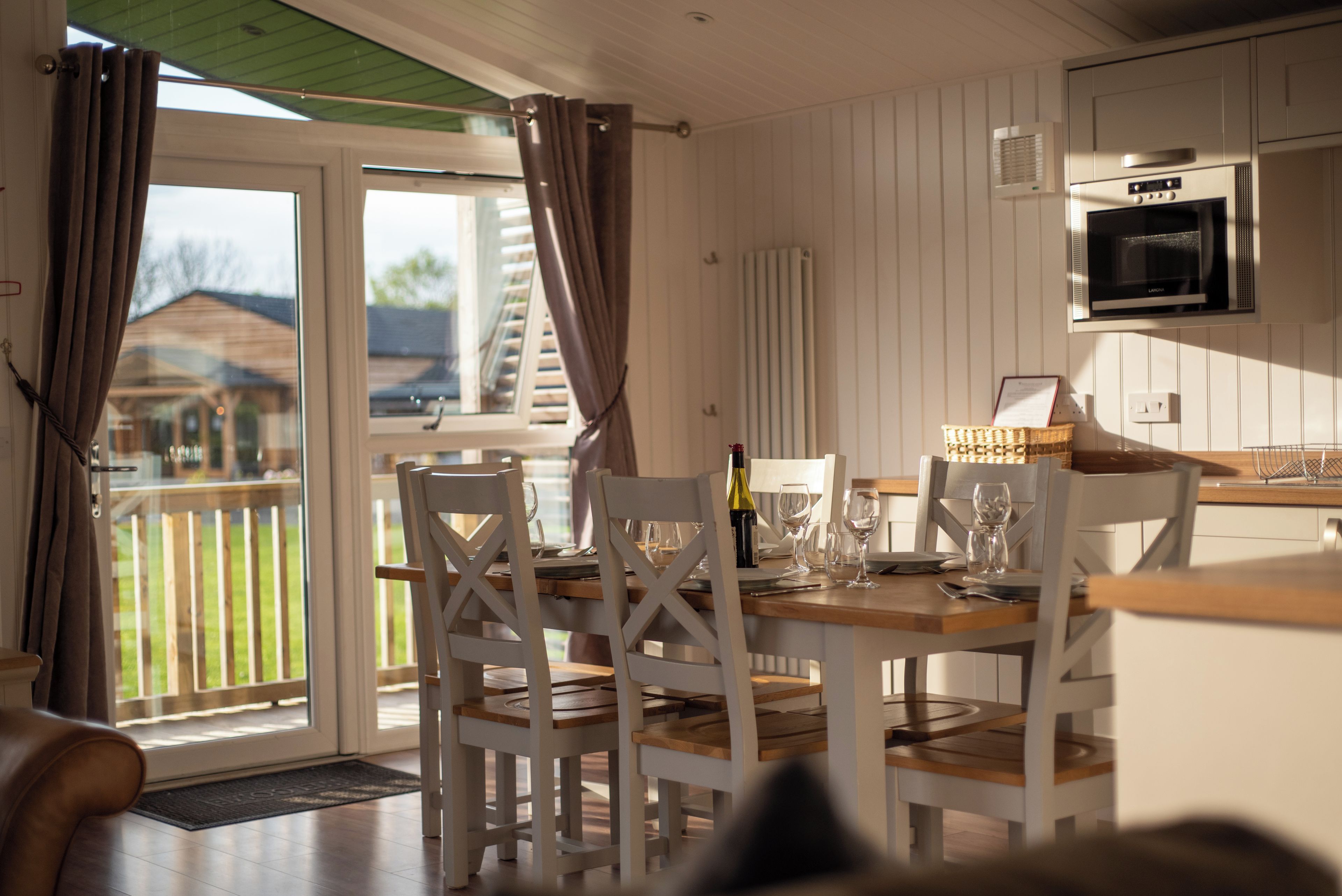 A dining area with a table set for four, a bottle of wine, and a view of the outdoors through a sliding glass door.