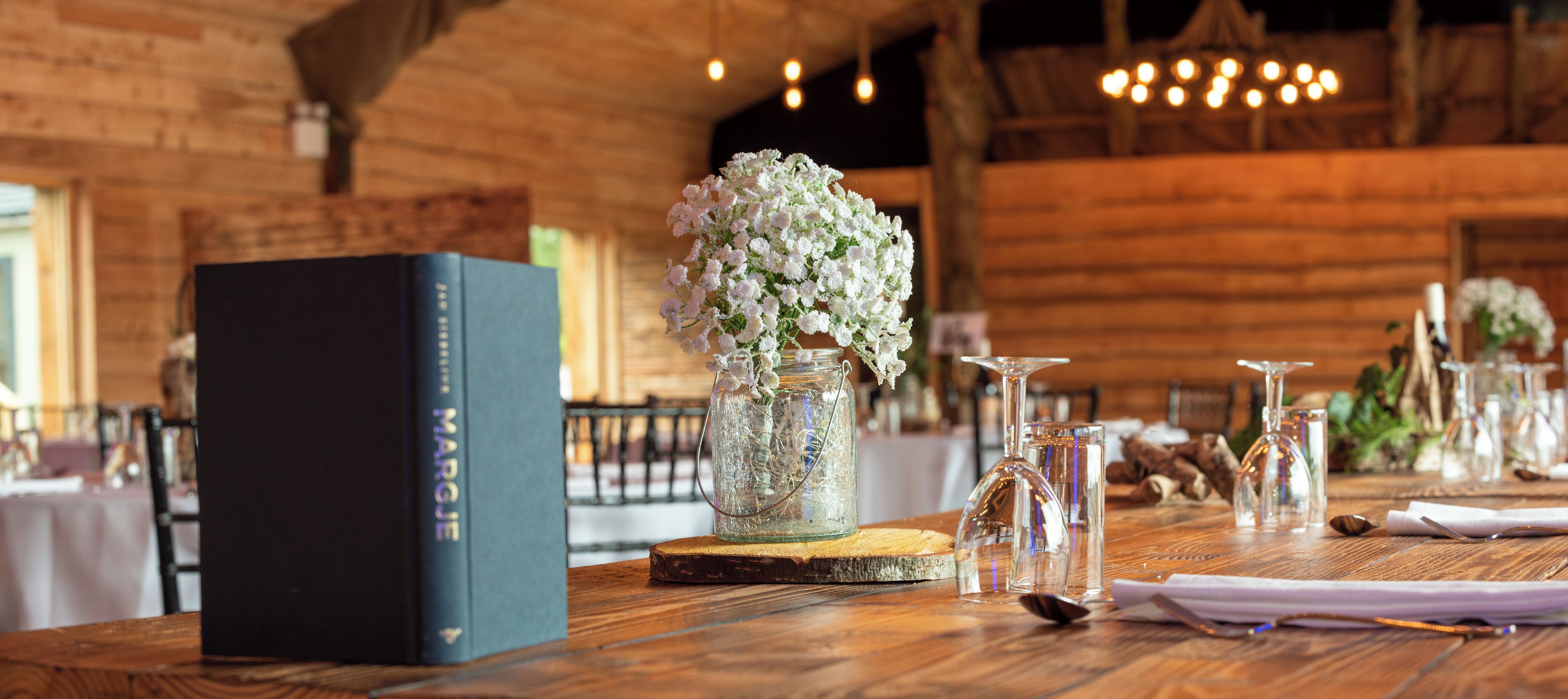 A wooden table with a book titled 'MARGUE' and a glass jar with white flowers.