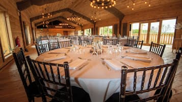 A large round table set for dining with chairs, wooden walls, and a chandelier.