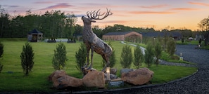 A deer sculpture in a landscaped area with a gazebo, a building, and a gravel path.