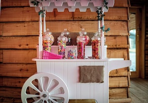 Un kiosque à bonbons avec des bocaux remplis de confiseries variées et une brouette blanche.
