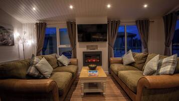 A cozy living room with two leather sofas, a coffee table, a flat-screen TV, and a fireplace.