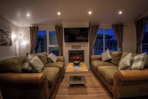 A cozy living room with two leather sofas, a coffee table, a flat-screen TV, and a fireplace.