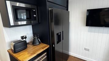 A compact kitchen with a microwave, toaster, kettle, and refrigerator.