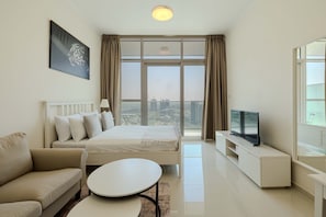 A modern hotel room with a bed, a sofa, a TV, and a large window offering a city view. - Modern Studio  Golf Views   DAMAC Hills 1 (Dubai)