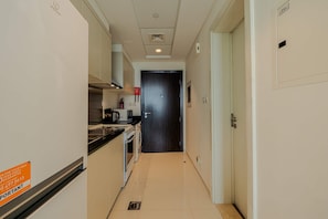 A narrow hallway with a kitchen area on one side, a dark wooden door at the end, and a white wall with a fire safety sign. - Modern Studio  Golf Views   DAMAC Hills 1 (Dubai)