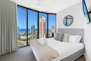 Ein Hotelzimmer mit einem großen Bett, einem runden Spiegel und Blick auf Stadt und Meer.