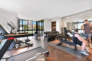 Een fitnessruimte met trainingsapparatuur, een loopband en een roeimachine.