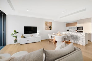 A modern living room with a flat-screen TV, dining area, and kitchen. - Jewel 27 Luxury 5 Star Beachfront King & Queen (Surfers Paradise)