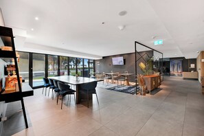 Ein geräumiger Innenbereich mit einem großen Tisch und Stühlen, einem Sofa und einem an der Wand befestigten Fernseher.