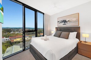 A hotel room with a large bed, a painting, and a view of a cityscape. - Tranquillity at Encore 2BR Sea & Hinterland Views (Broadbeach)