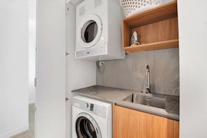 A compact laundry area with a front-loading washing machine and a top-loading dryer. - Tranquillity at Encore 2BR Sea & Hinterland Views (Broadbeach)