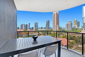A balcony with a table and chairs, overlooking a cityscape with high-rise buildings. - Tranquillity at Encore 2BR Sea & Hinterland Views (Broadbeach)