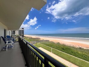 A balcony with a view of a beach, a shuffleboard, and a building in the background. - 'The Pelican Soleil Condo' on the beach! (Ormond Beach)