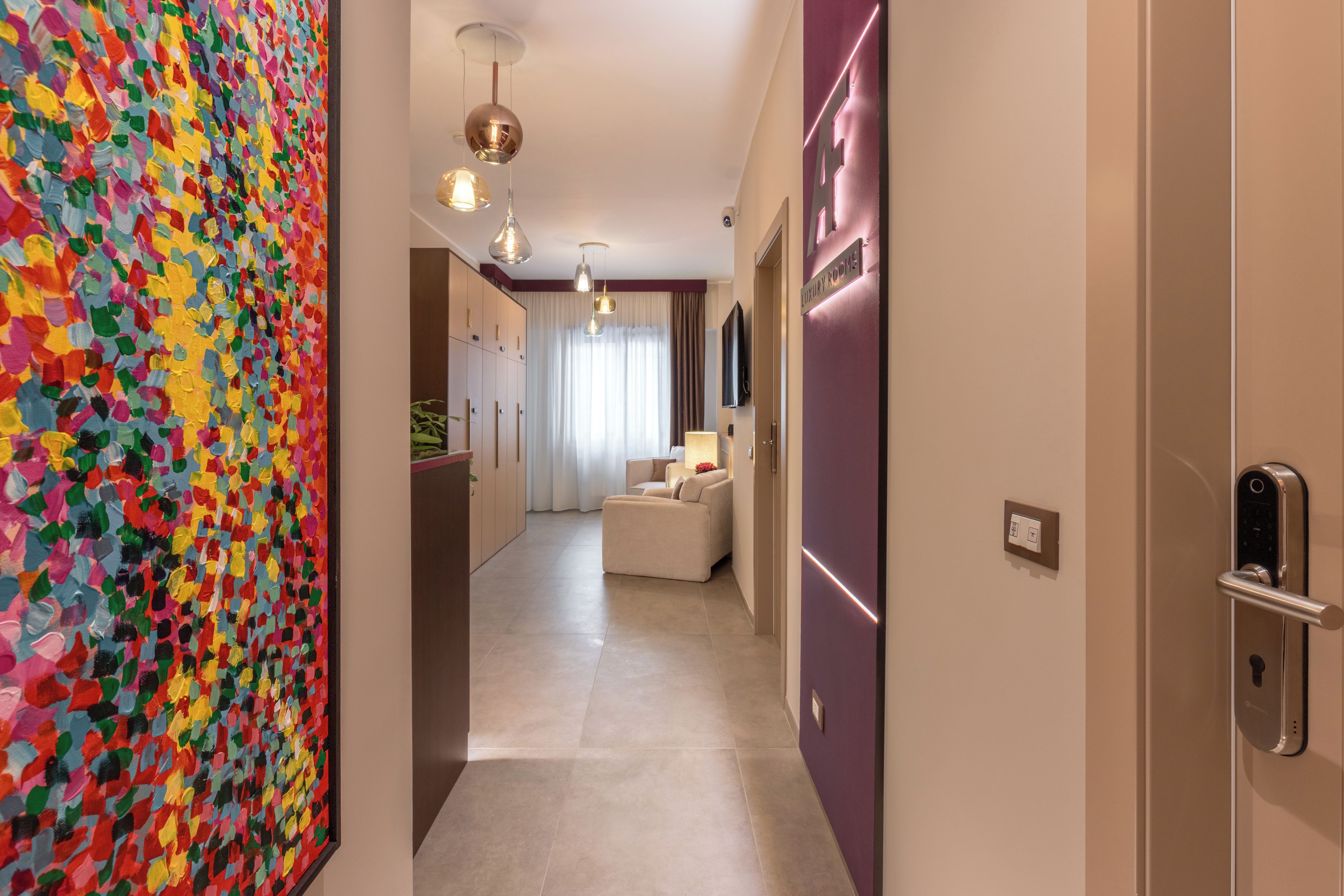 A hallway with a colorful abstract painting on the left, a modern light fixture, and a sign indicating 'LUXURY ROOMS' on the right.