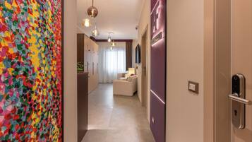 Un pasillo con un cuadro abstracto de colores vibrantes a la izquierda, un moderno aparato de luz y un cartel que indica 'LUXURY ROOMS' a la derecha.
