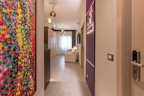Um corredor com uma pintura abstrata colorida à esquerda, uma luminária moderna e uma placa indicando 'LUXURY ROOMS' à direita.