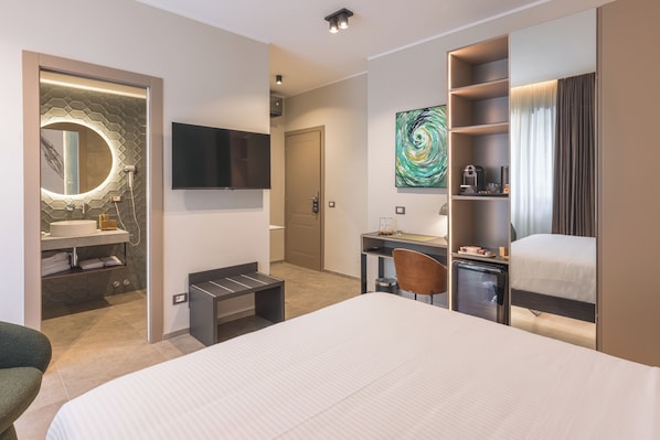 Habitación de hotel moderna con una cama grande, un escritorio, un televisor, un baño con espejo y lavabo, y un cuadro en la pared.