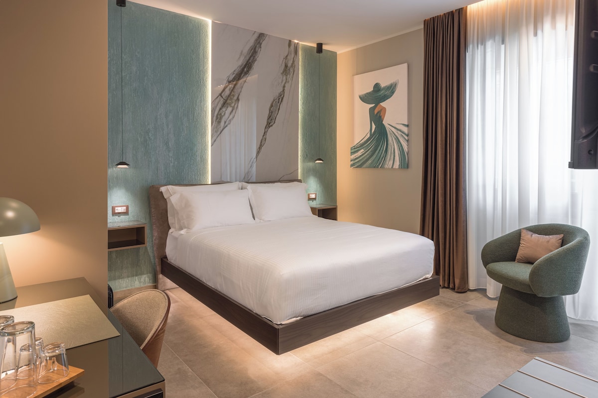 Quarto de hotel moderno com uma cama grande, um espaço de estar com uma poltrona e obras de arte nas paredes.