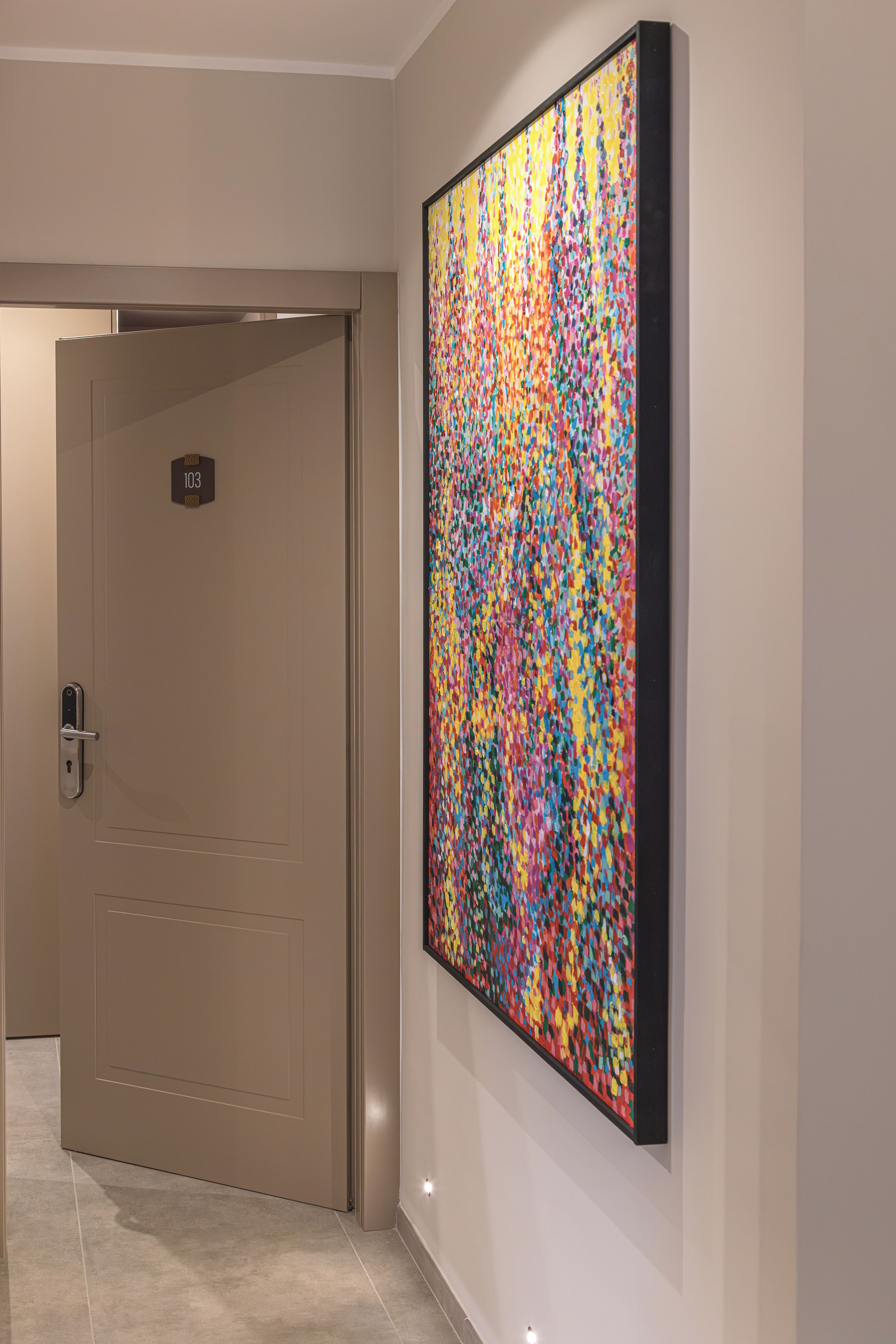 A hallway with a door marked '103' and a colorful abstract painting on the wall.