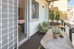 A balcony with a seating area, a potted plant, and a view of the street.