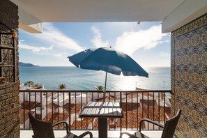 A balcony with a table and chairs, overlooking a coastal view with the sea and distant land. - Apartment in Nerja Near Carabeillo Beach (Nerja)
