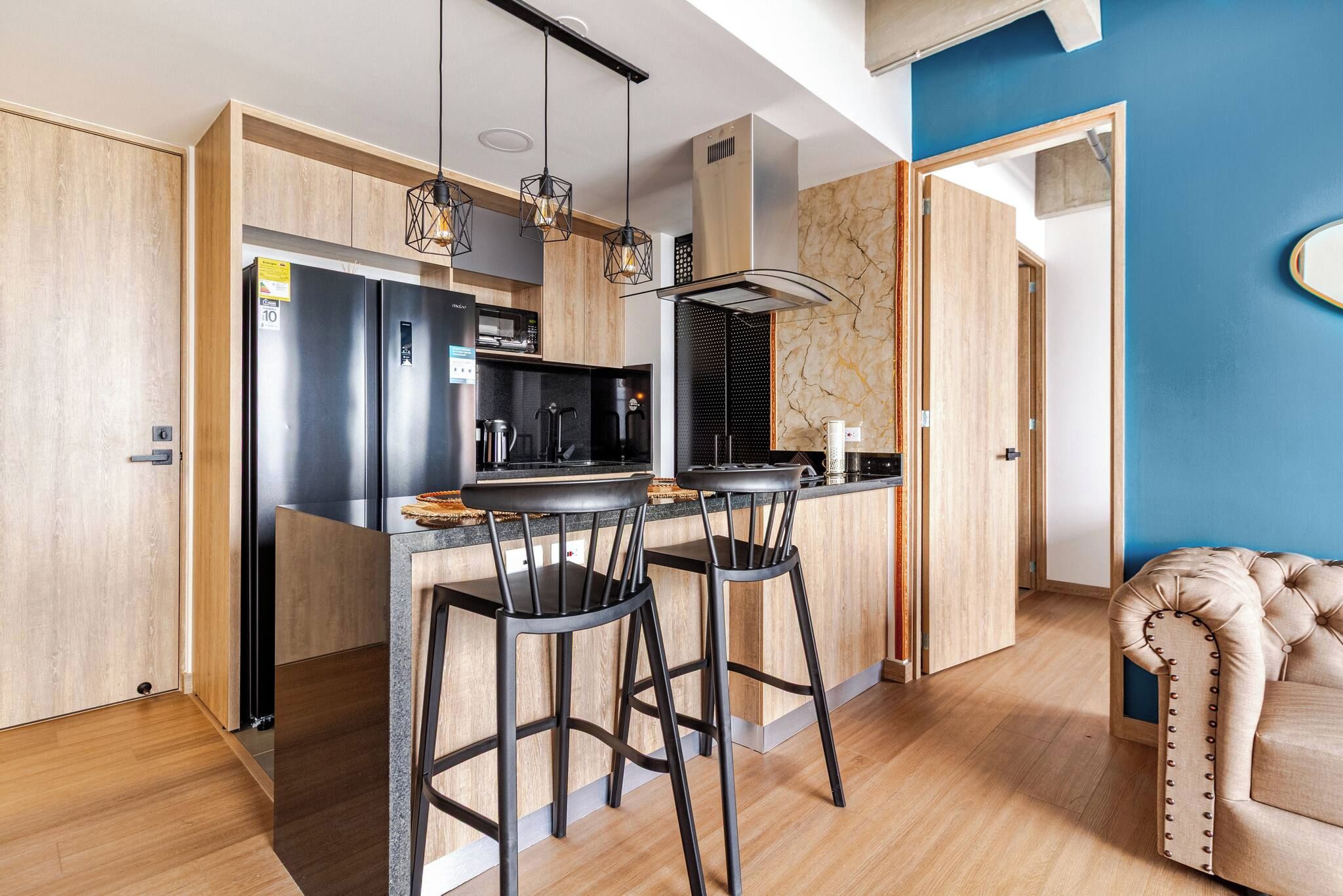 A modern kitchen with a central island, bar stools, a stainless steel refrigerator, and a microwave.