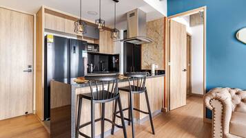 A modern kitchen with a central island, bar stools, a stainless steel refrigerator, and a microwave.