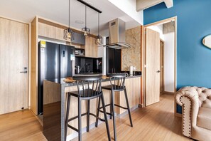 Cocina moderna con una isla central, taburetes de bar, un refrigerador de acero inoxidable y un microondas.
