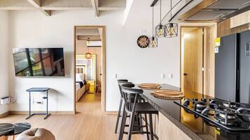 A modern kitchen with a gas stove, bar stools, and a large flat-screen TV.