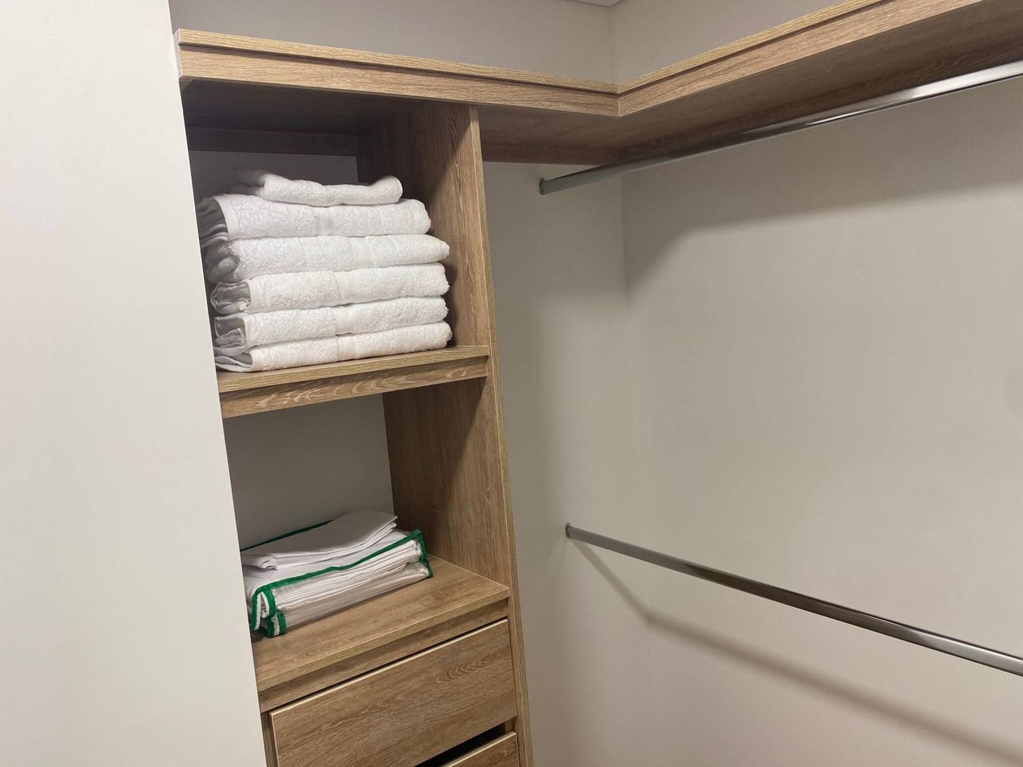 Un armario con estantes y cajones de madera, que contiene toallas dobladas y una bolsa verde.