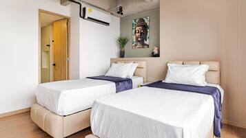 Habitación de hotel con dos camas, unidad de aire acondicionado en el techo, una puerta y una obra de arte colgada en la pared.