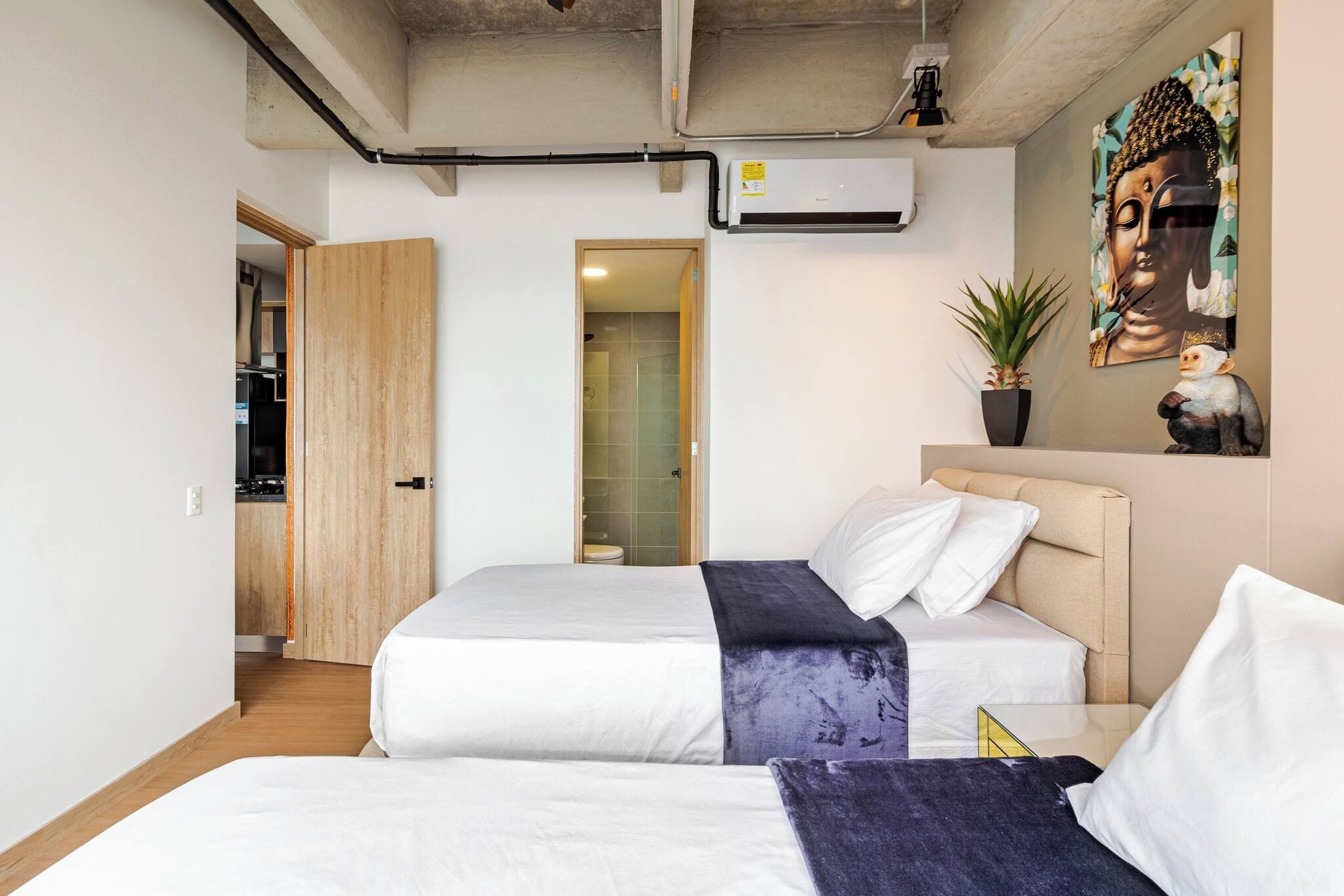 Habitación de hotel con una cama, una mesita de noche, una planta en maceta y un aire acondicionado instalado en la pared.