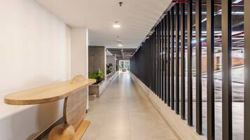 A corridor with a reception desk, potted plants, and a view of the parking area through a glass wall.