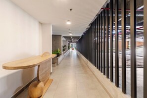 Un pasillo con mostrador de recepción, plantas en macetas y vista al estacionamiento a través de un muro de vidrio.