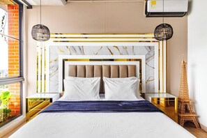 Un dormitorio moderno con cabecera de mármol, cama con ropa de cama blanca y una réplica decorativa de la Torre Eiffel.