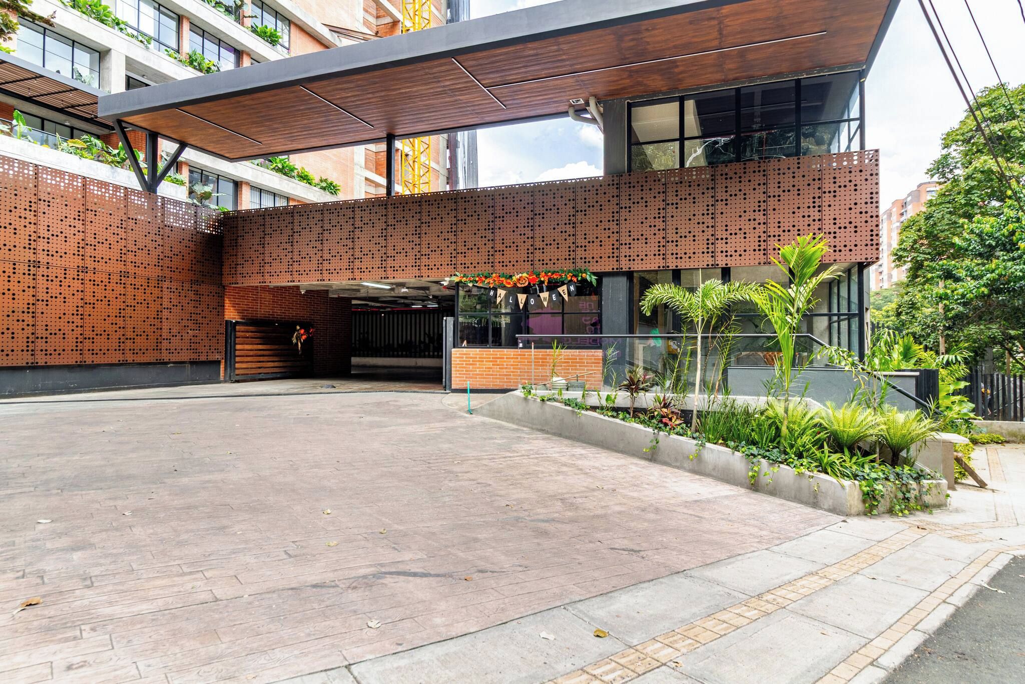 A modern building with a covered entrance, a brick facade, and a landscaped area with plants.