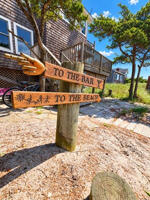 Et træskilt med piletavler, der viser vejen til baren og stranden.
