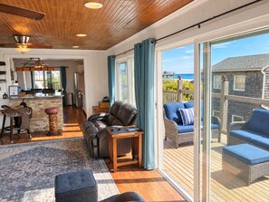 A spacious living area with a large sliding glass door leading to an outdoor deck, a leather sofa, and a bar area. - Gatsby’s OBP, 3rd House to the Beach, Heated Pool + 2 Hot Tubs, Sleeps 24 (Ocean Bay Park)