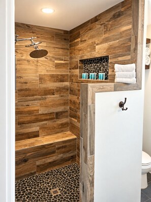Une salle de bain moderne avec un mur décoré en bois, une douche dotée d’un pommeau de douche à pluie et des toilettes.