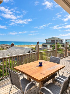 Une terrasse en bois avec une table et des chaises, donnant sur une plage et l’océan.