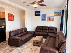 A living room with a brown leather sofa, a wooden coffee table, and a ceiling fan. - Gatsby’s OBP, 3rd House to the Beach, Heated Pool + 2 Hot Tubs, Sleeps 24 (Ocean Bay Park)