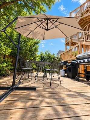 En udendørs terrasse med et bord, stole, en stor parasol og en grill.
