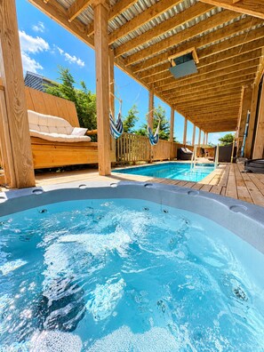 Une terrasse en bois avec un jacuzzi, une chaise longue et une piscine.