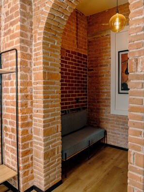 Quarto com paredes de tijolos aparentes, um banco, luminária pendente e um quadro na parede.