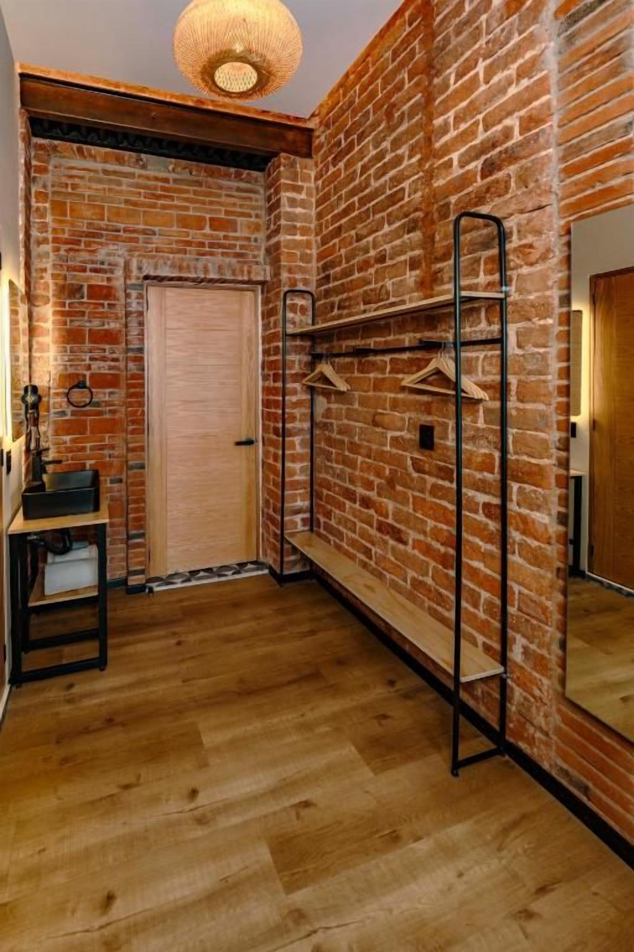 A room with a brick wall, wooden floor, a coat rack, and a door.